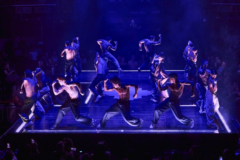 Shirtless male dancers perform choreographed routines on a stage under blue stage lighting during Magic Mike Live stage show.